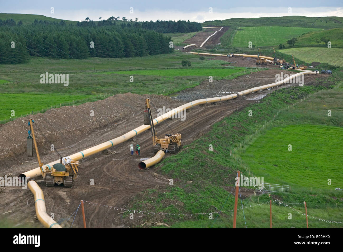 Sezioni di diametro grande trasmissione gas pipeline in acciaio infilati attraverso il paesaggio prima di essere uniti tra di loro e sepolto Foto Stock
