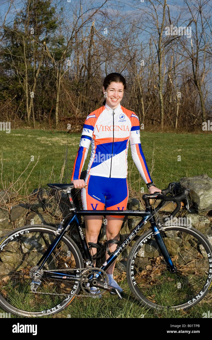 Ritratto di college di età giovane femmina ciclista in piedi con la bici vestito in arancione blu e bianco con kit di cielo blu sullo sfondo Foto Stock