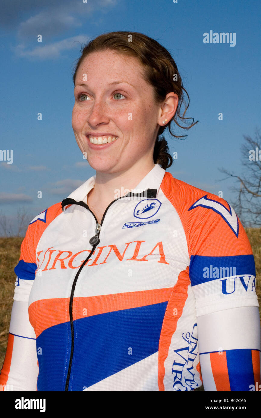 Ritratto di un collegio di età giovane femmina ciclista vestito in arancione, blu e bianco con kit di cielo blu sullo sfondo. Foto Stock