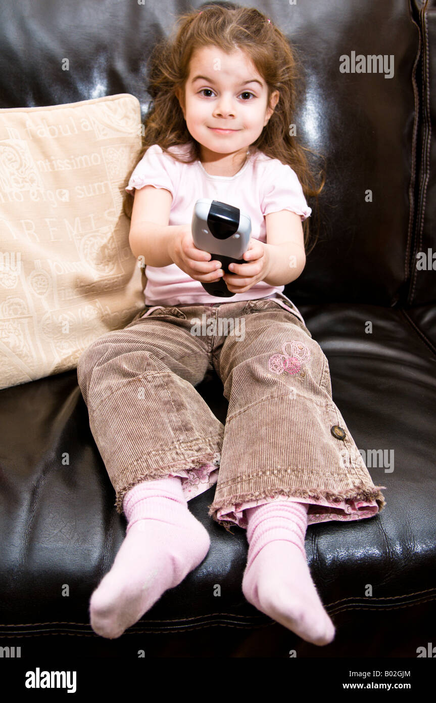 Una bambina di 4 anni dimostra l'uso di un telecomando di un televisore mentre la visualizzazione di televisione Foto Stock