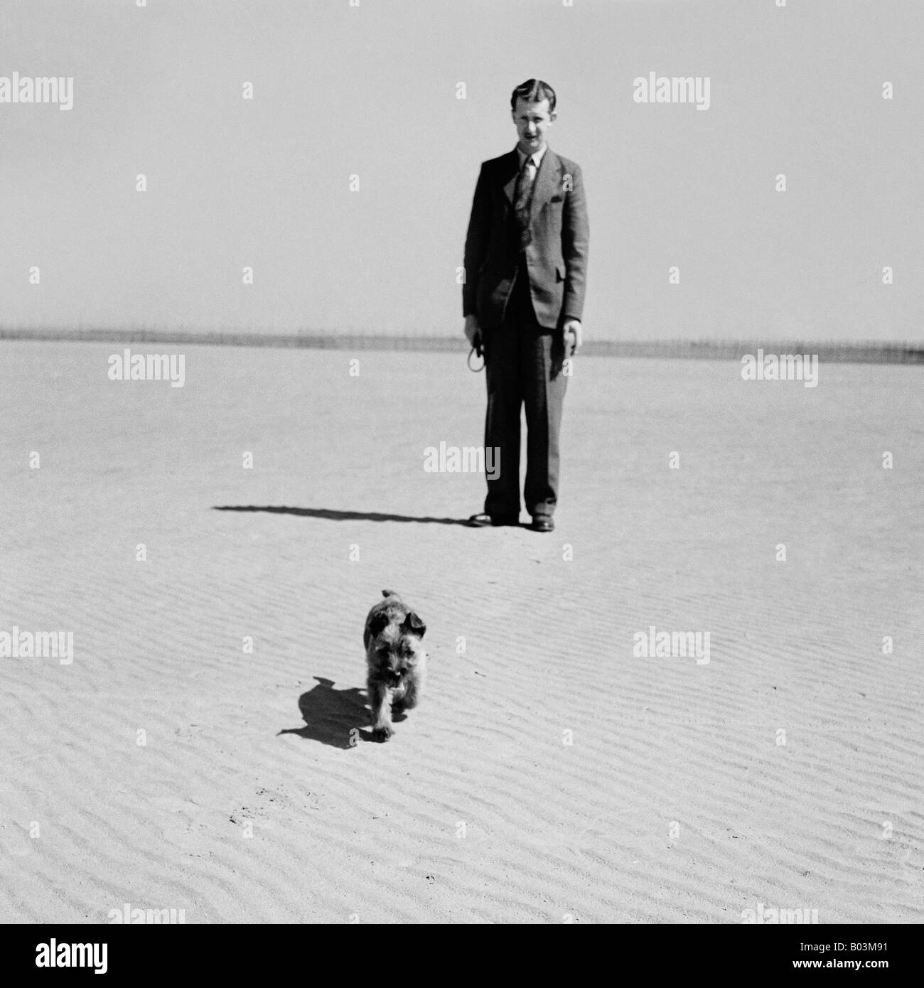 Vecchia famiglia vintage fotografia istantanea dell'uomo con piccoli terrier cucciolo di cane che corre sulla spiaggia Foto Stock