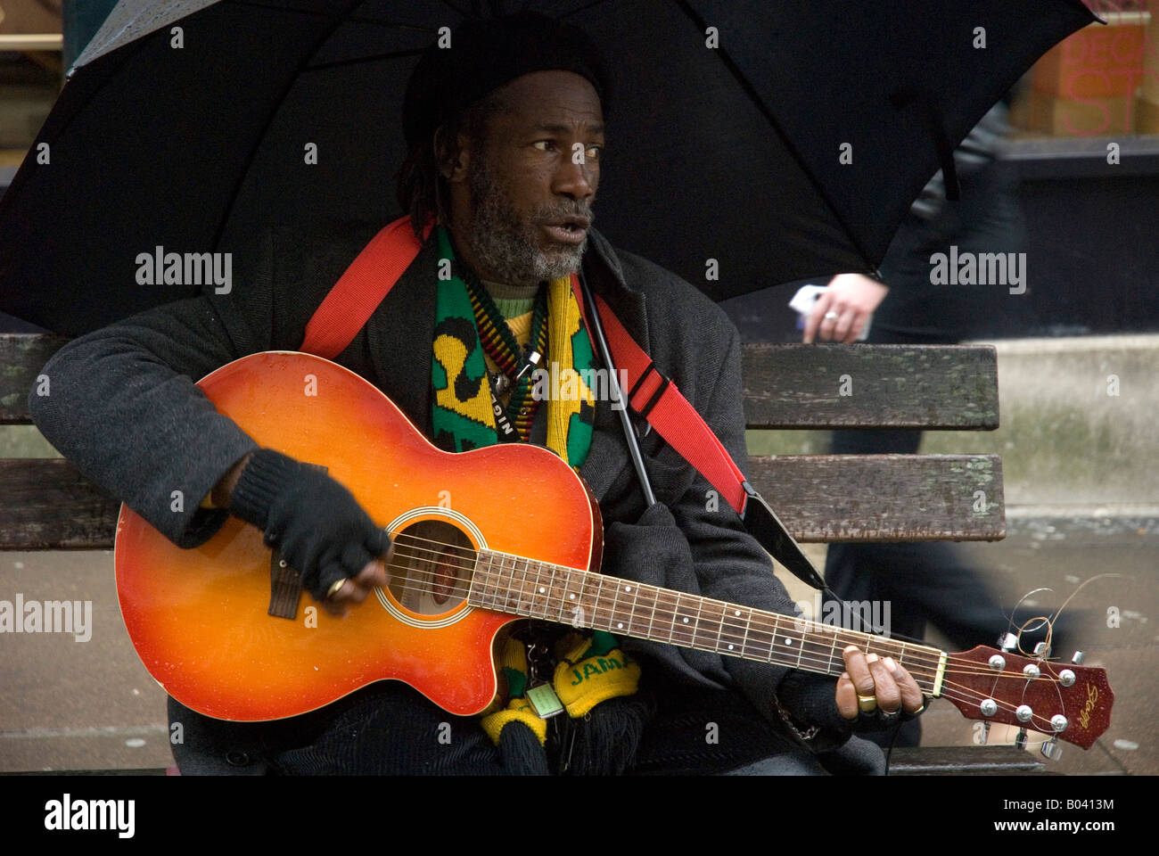 Il giamaicano musicista di strada seduta su una panchina sotto un ombrello a suonare la chitarra, bagno, Somerset, Inghilterra, Regno Unito Foto Stock