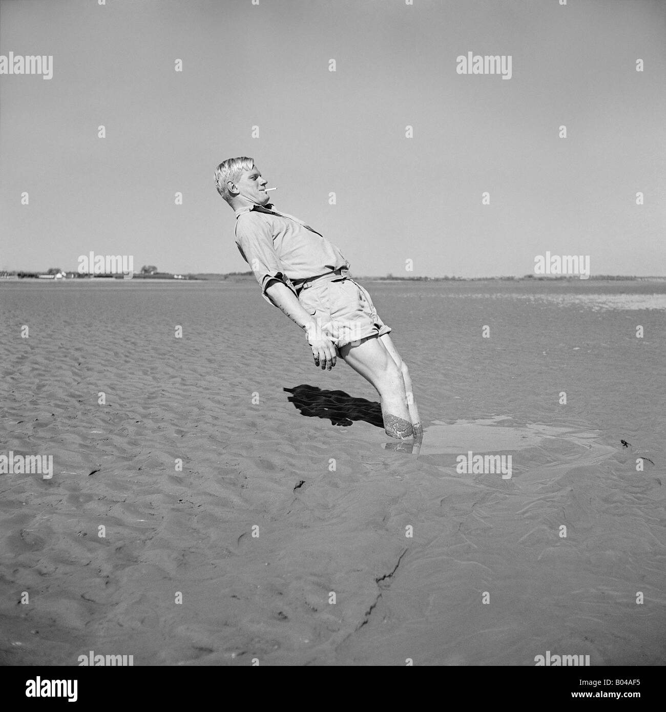 Vecchio vintage snapshot dell uomo che indossa pantaloncini in piedi nel fango sulla spiaggia Foto Stock