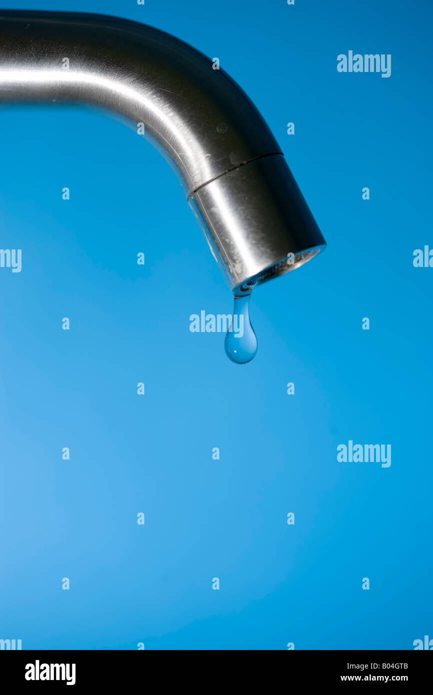 Close-up di una goccia di acqua appesa da un rubinetto, sfondo blu Foto Stock