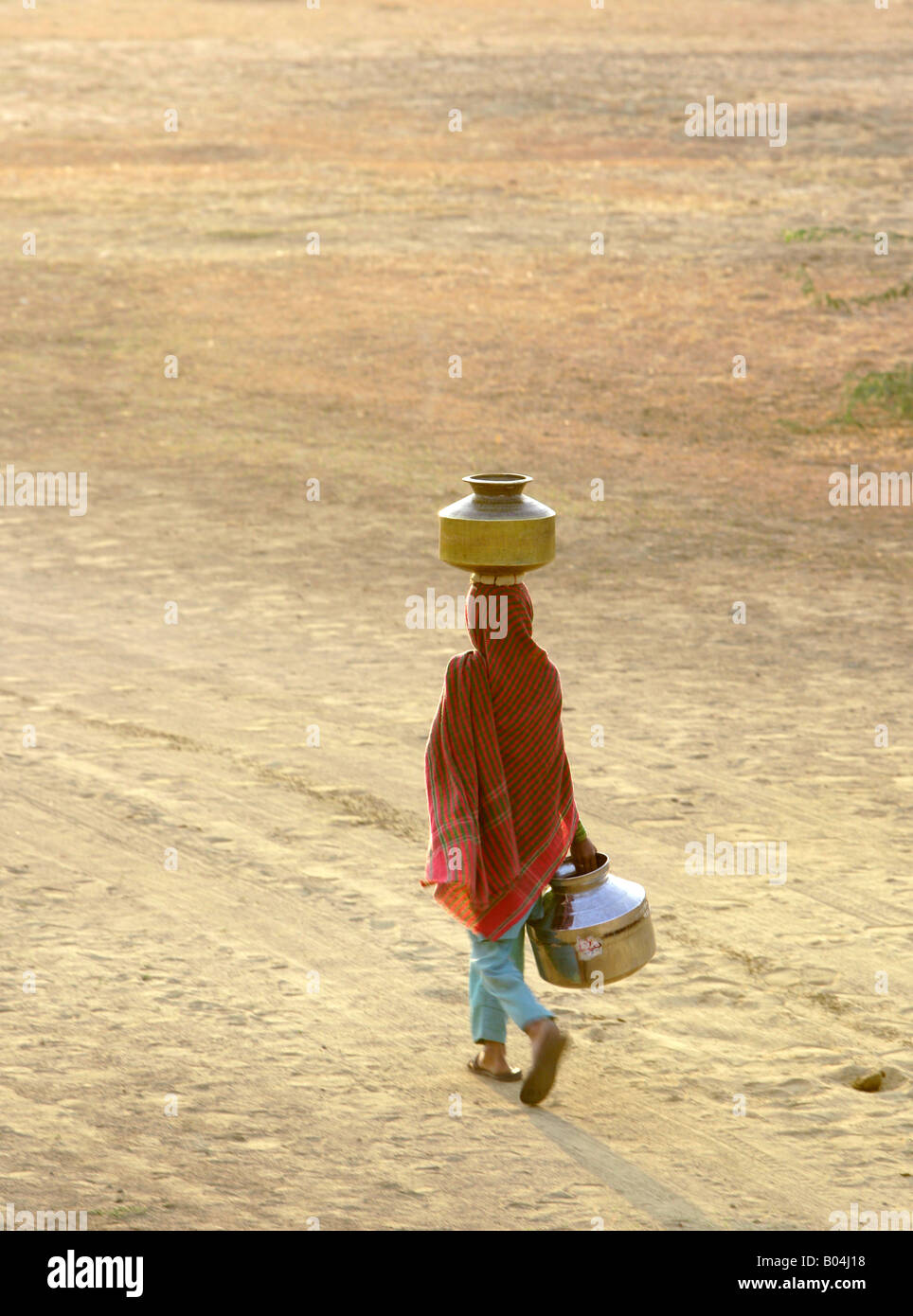 Giovane ragazza il recupero di acqua e il bilanciamento di un contenitore sul suo capo, vicino a Jaisalmer, Rajasthan, India Foto Stock