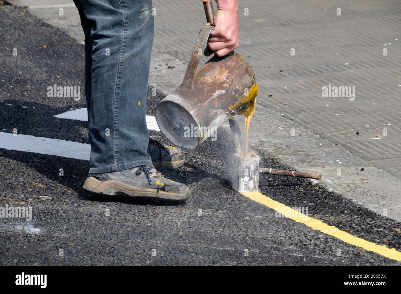 Workman versando giallo caldo marcatura linea liquido in ferro dispensatore di attrezzo Foto Stock