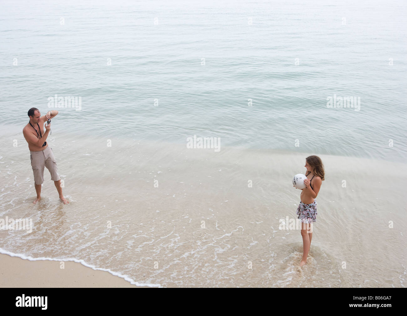 L uomo si prende la foto di una ragazza giovane con la palla sulla spiaggia Foto Stock