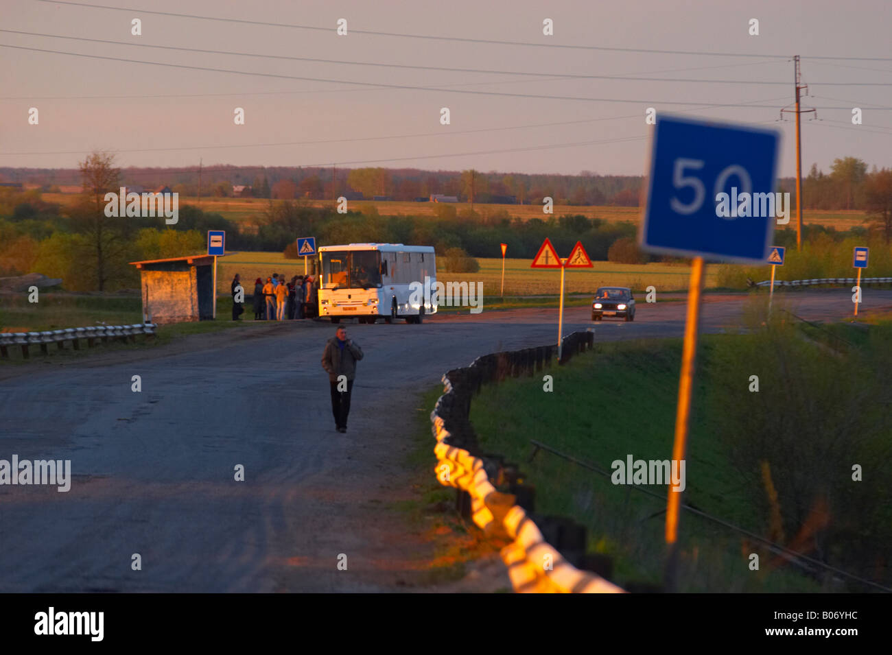 Persone su un autobus al tramonto in provinciale città russa di Gruzino nella regione di Novgorod. Vecchia strada con cartelli stradali Foto Stock