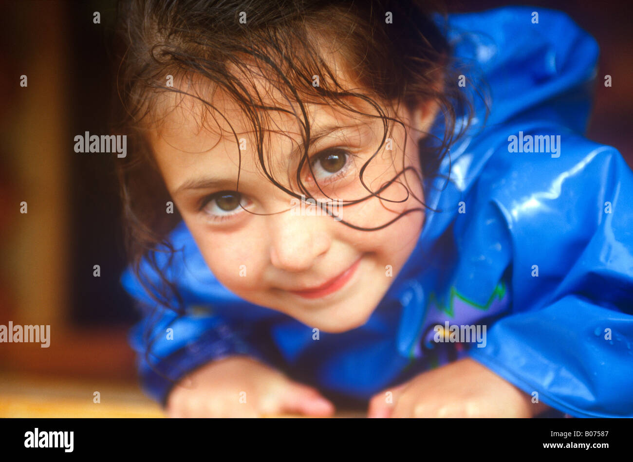 Un timido bambino con ricci, gli occhi grandi e indossando un blu brillante impermeabile Foto Stock
