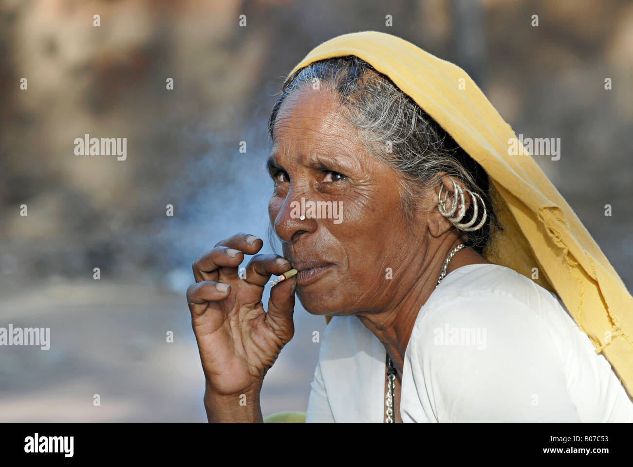 Vecchia donna tribale che fuma bidi, una sigaretta indiana fatta a mano di tabacco o foglie di beedi. Tribù Bhil facce rurali dell'India Foto Stock