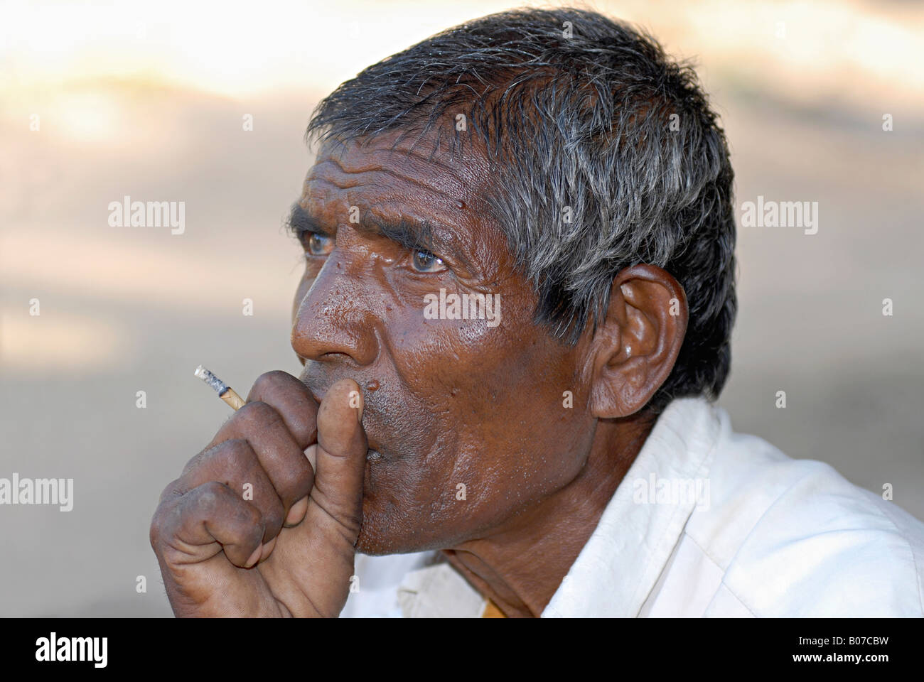 Primo piano di un uomo tribale di Bhil che fuma una sigaretta indiana fatta a mano di foglie di tabacco. Facce rurali dell'India Foto Stock