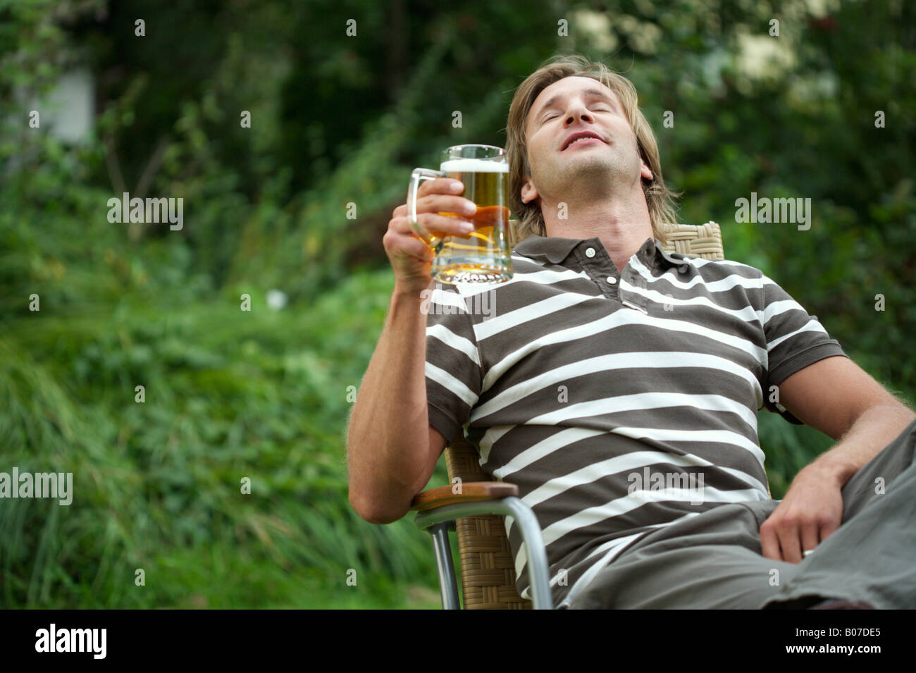 Uomo con in mano un bicchiere di birra seduti in un prato sedia Foto stock  - Alamy