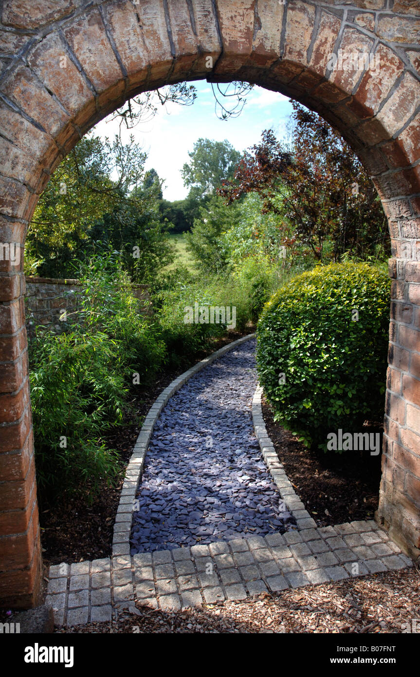 Un arco in pietra che conduce a un giardino percorso posati con frammenti di ardesia e bordato con ciottoli di granito Foto Stock