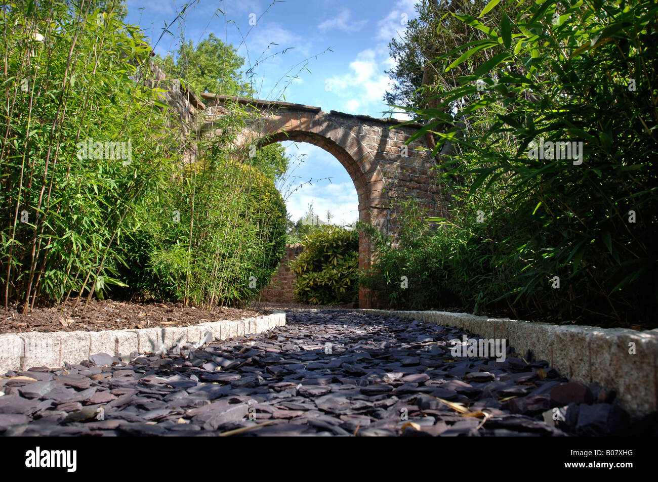 Un arco in pietra che conduce a un giardino percorso posati con frammenti di ardesia e bordato con ciottoli di granito Foto Stock