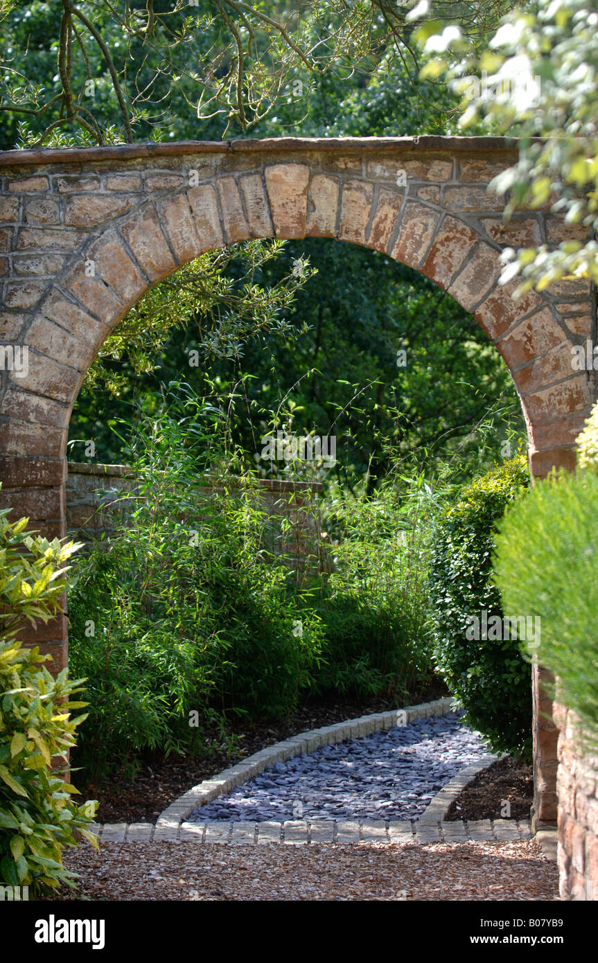 Un arco in pietra che conduce a un giardino percorso posati con frammenti di ardesia e bordato con ciottoli di granito Foto Stock