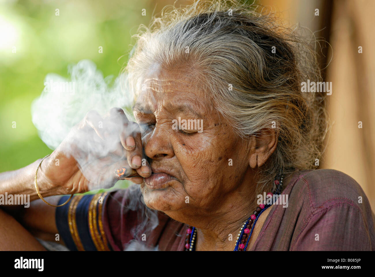 Primo piano di una vecchia donna fumatori bidi, un indiano a mano fatte di sigarette di tabacco o beedi foglie. Warli tribe Foto Stock