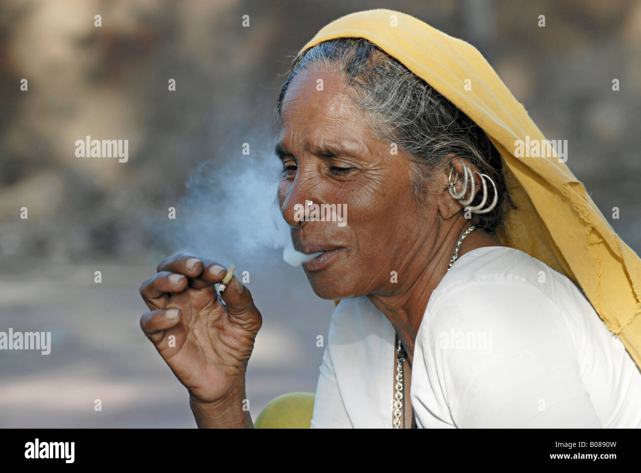 Vecchia donna tribale che fuma bidi, una sigaretta indiana fatta a mano di tabacco o foglie di beedi. Tribù Bhil. Facce rurali dell'India Foto Stock