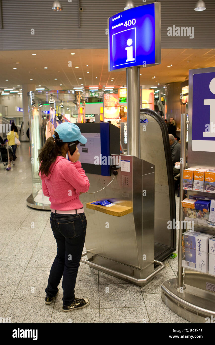 Giovane donna di effettuare una chiamata a un punto di informazione nel Terminal 1 dell'aeroporto internazionale di Francoforte Hesse, Germania Foto Stock