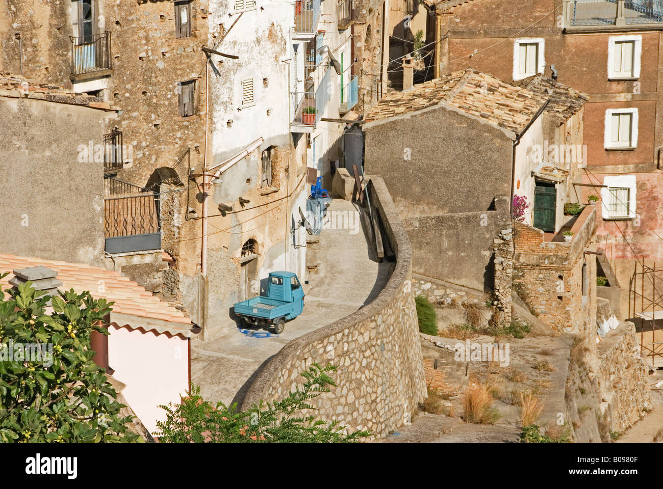 Blu a tre ruote scooter di consegna su una stretta strada di montagna in una ripida montagna villaggio, Povalino, Calabria, meridionale Foto Stock