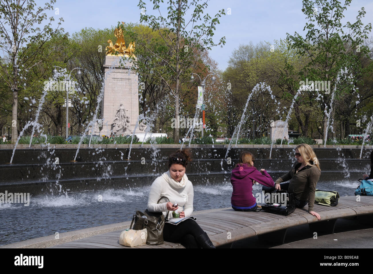 A Columbus Circle in midtown Manhattan la gente mangia, chiacchierare e rilassarsi accanto alla fontana. Dietro di loro è Central Park. Foto Stock