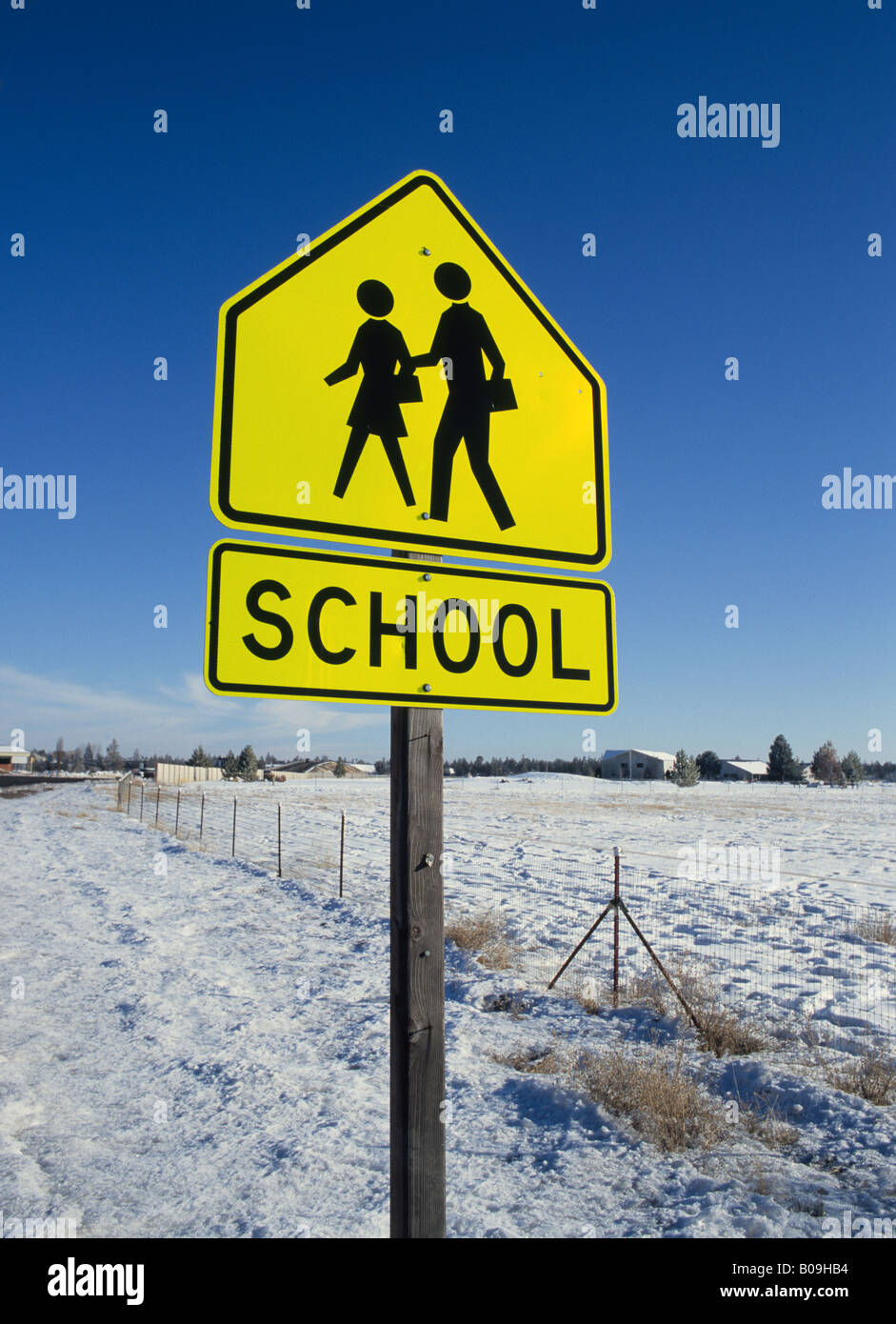 Un segno di scuola su una autostrada che mette in guardia i visitatori a fermarsi e resa ai bambini attraversando la strada Foto Stock