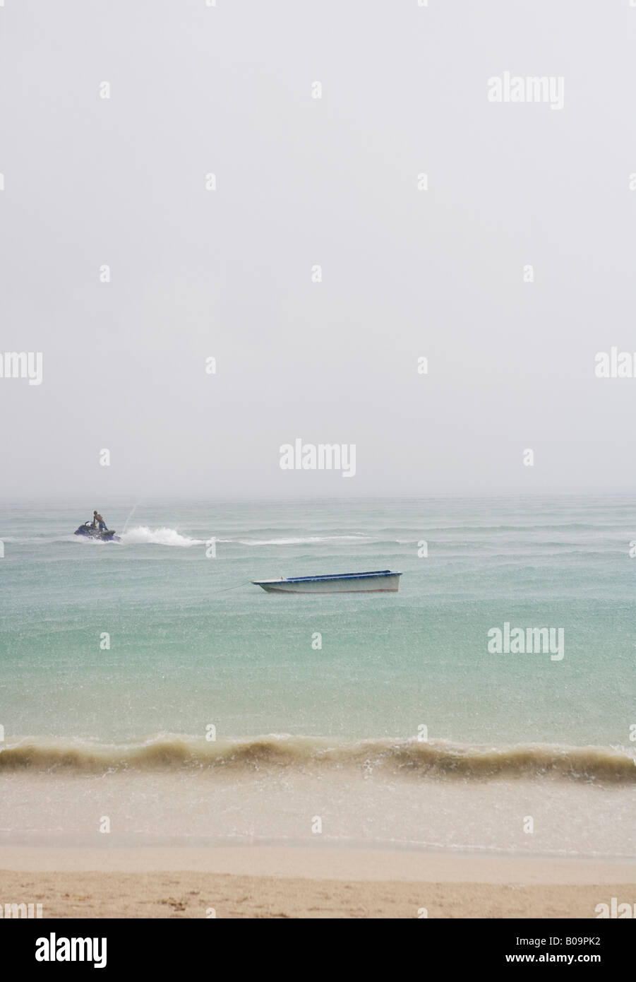 Una barca ancore su di una spiaggia di sabbia bianca, un jet-ski pass. Foto Stock