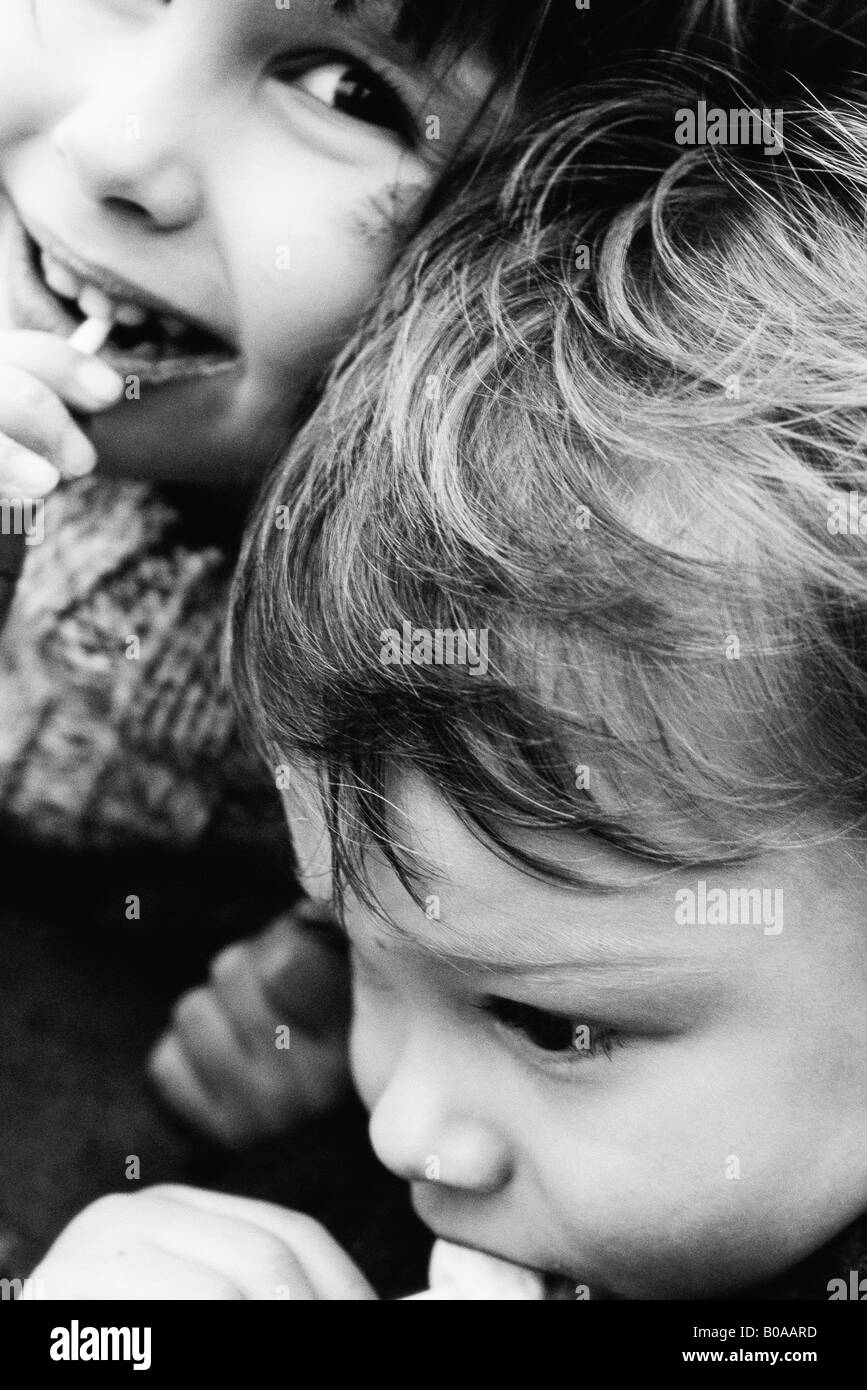 Due fratelli di mangiare lecca lecca, ragazza sorridente in telecamera, close-up Foto Stock