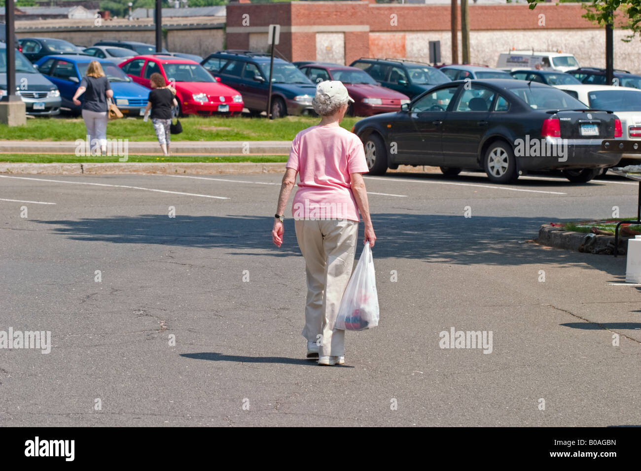 Medioevo Donna che cammina nel parcheggio portando un sacchetto di plastica Foto Stock