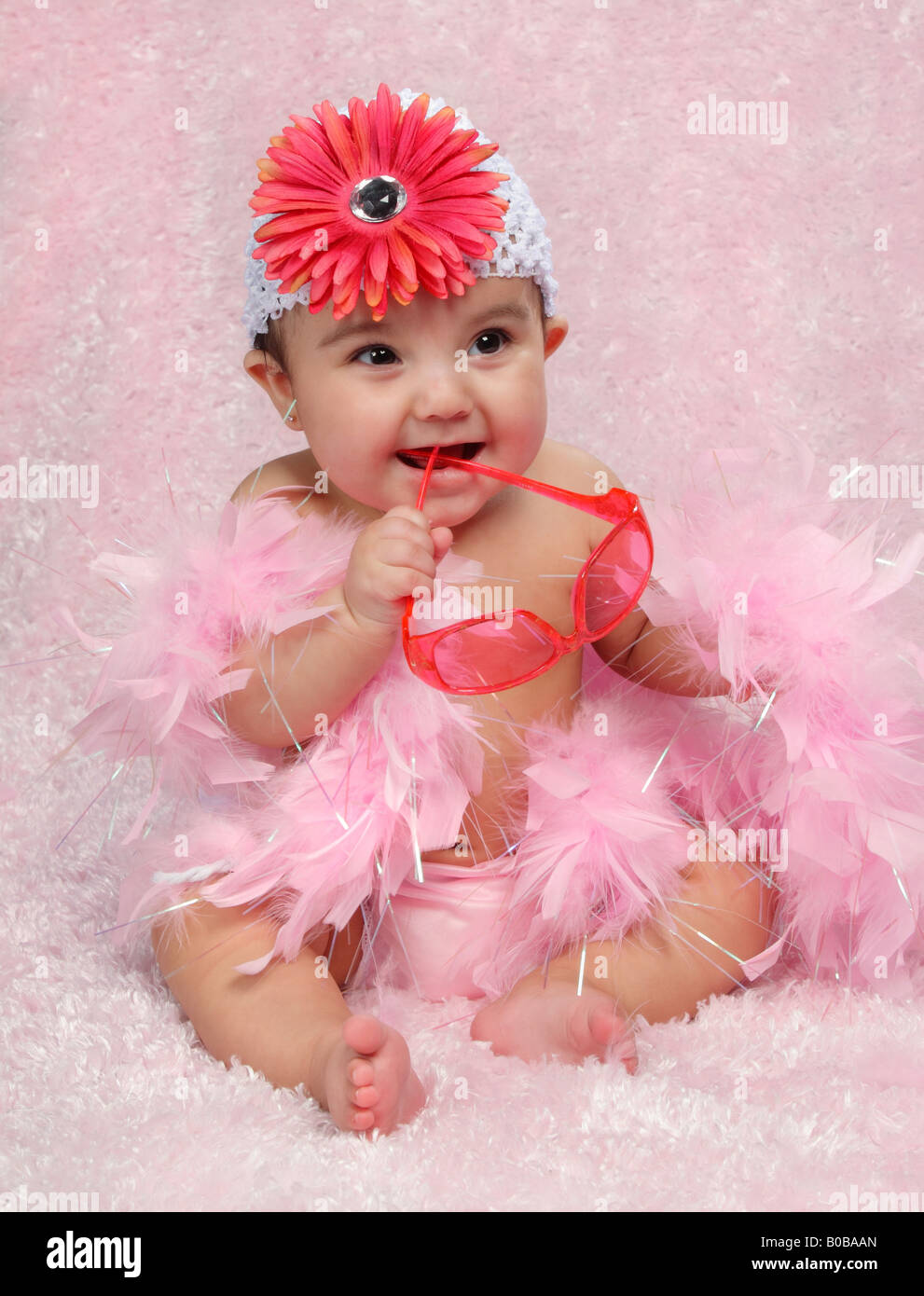 Piccola ragazza ispanica seduto e vestito in rosa con occhiali da sole e cappello di fiori Foto Stock