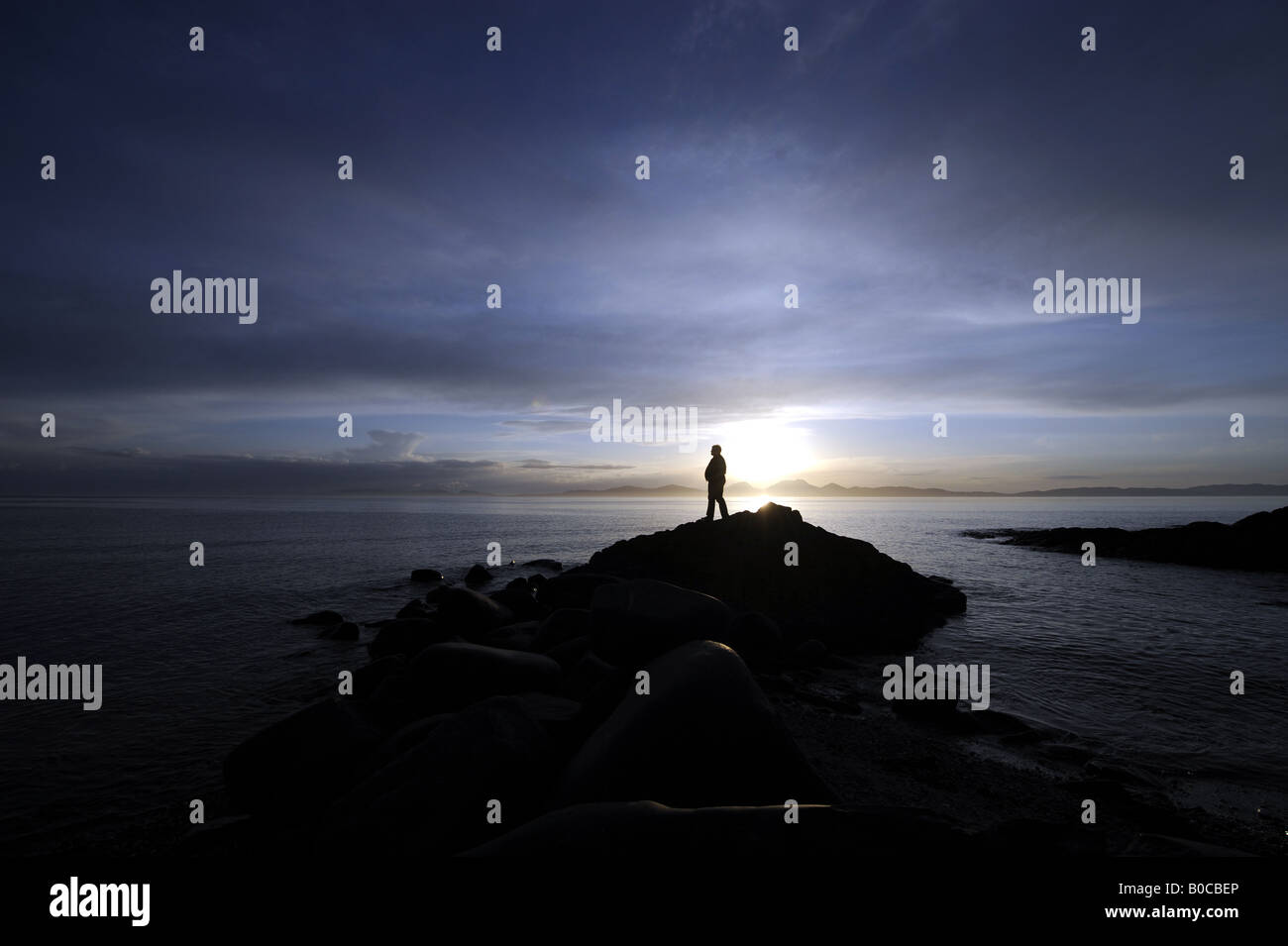 Una persona guarda un tramonto spettacolare sulla costa di Kintyre cercando di fronte all' isola di Jura,Scozia,UK. Foto Stock