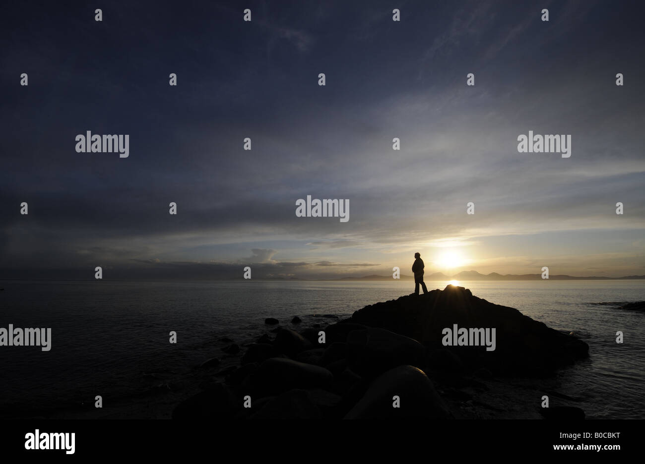 Una persona guarda un tramonto spettacolare sulla costa di Kintyre cercando di fronte all' isola di Jura,Scozia,UK. Foto Stock