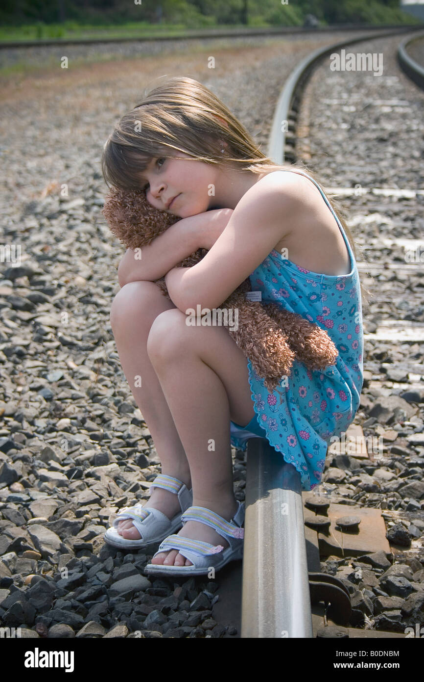 Lonely bambino siede sui binari del treno con il suo orsacchiotto Foto Stock