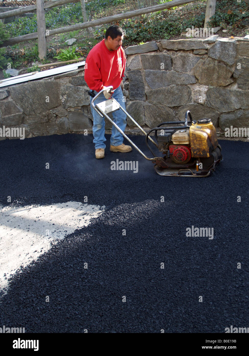 Giorno operaio stamping giù su asfalto appena costruito passo carraio Foto Stock