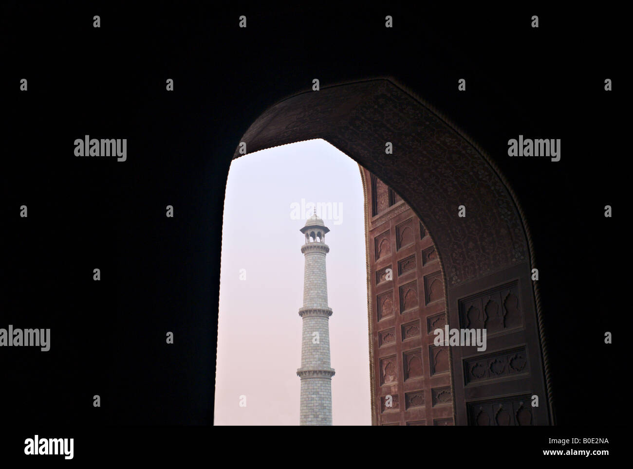 INDIA AGRA UN minarette del monumento del Taj Mahal si vede attraverso un arco di mattina nebbia di sunrise Foto Stock