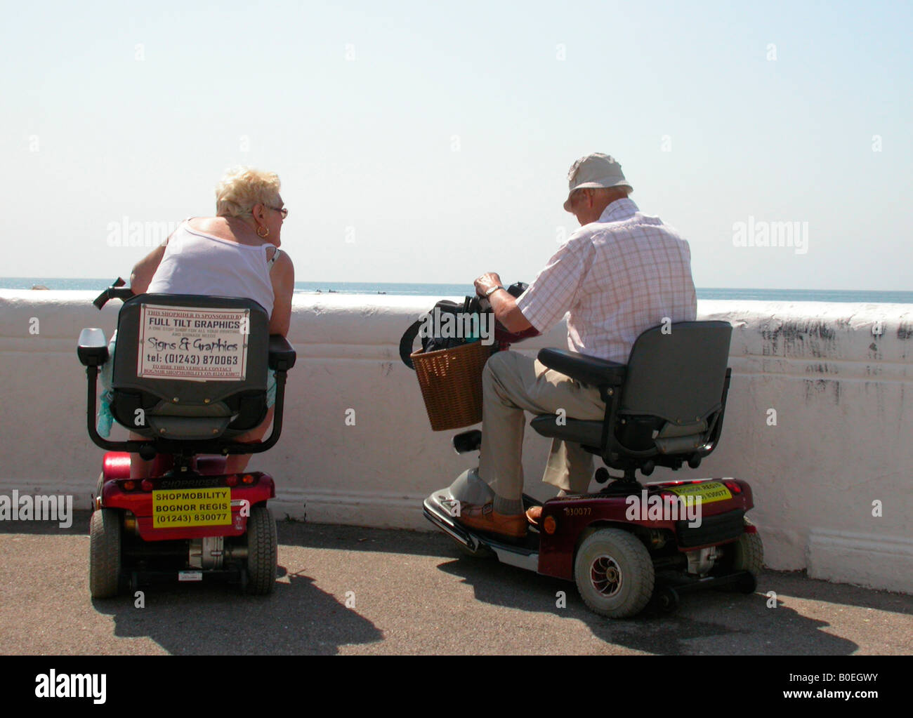 Coppia di anziani al mare ottenendo circa su elettronica scooter motorizzato sul prestito da Shopmobility Bognor Regis West Sussex Foto Stock