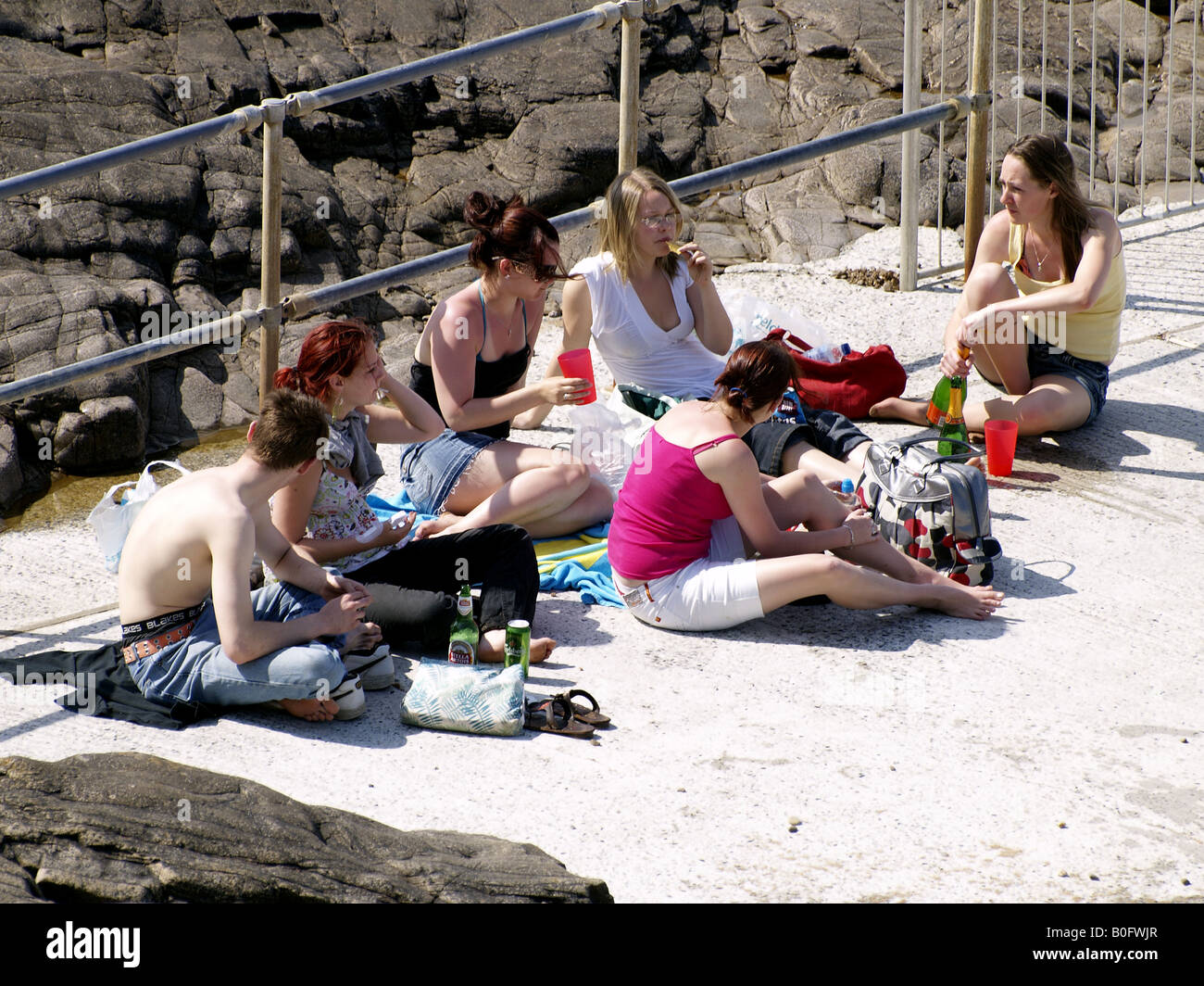 Gruppo di adolescenti seduta sul bordo di Bude seapool, mangiare e bere Foto Stock