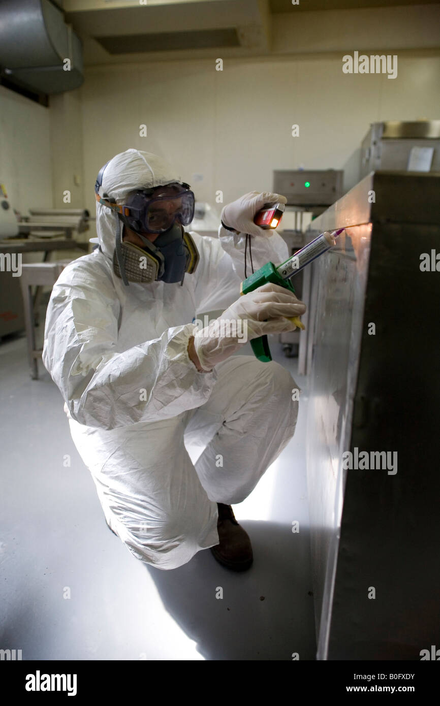 L uomo indossa uniformi di protezione guanti e maschera è la sterilizzazione di una superficie metallica Foto Stock