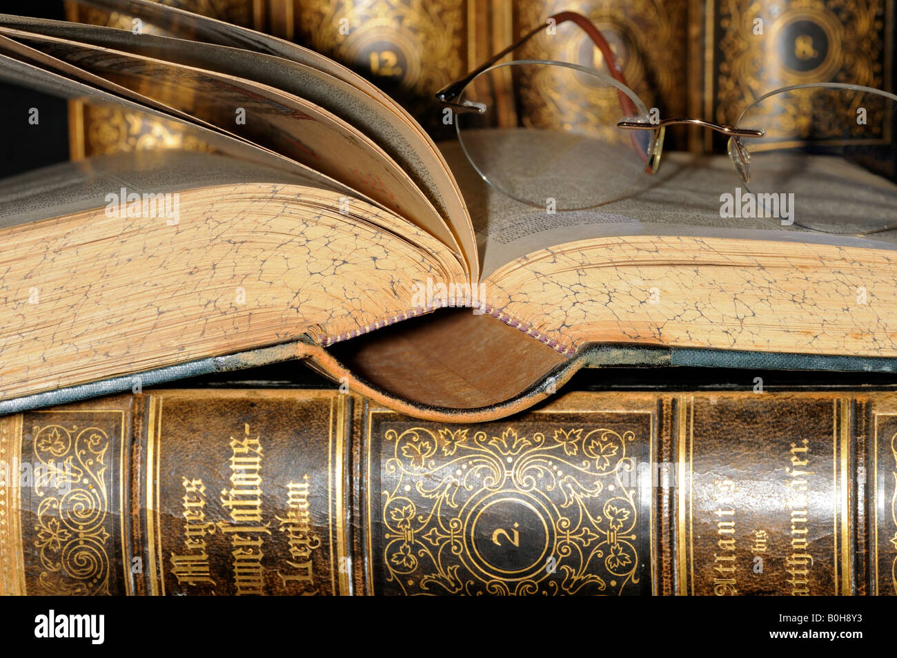 Gli occhiali da lettura in appoggio su una pagina aperta di una vecchia enciclopedia, pelle libri rilegati Foto Stock