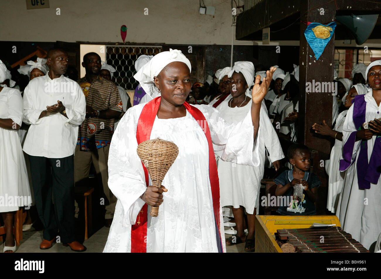 Donna vestito di vesti bianche e rosso anta a fare musica con un battito di vimini durante il servizio di una chiesa a Douala Camerun, Africa Foto Stock