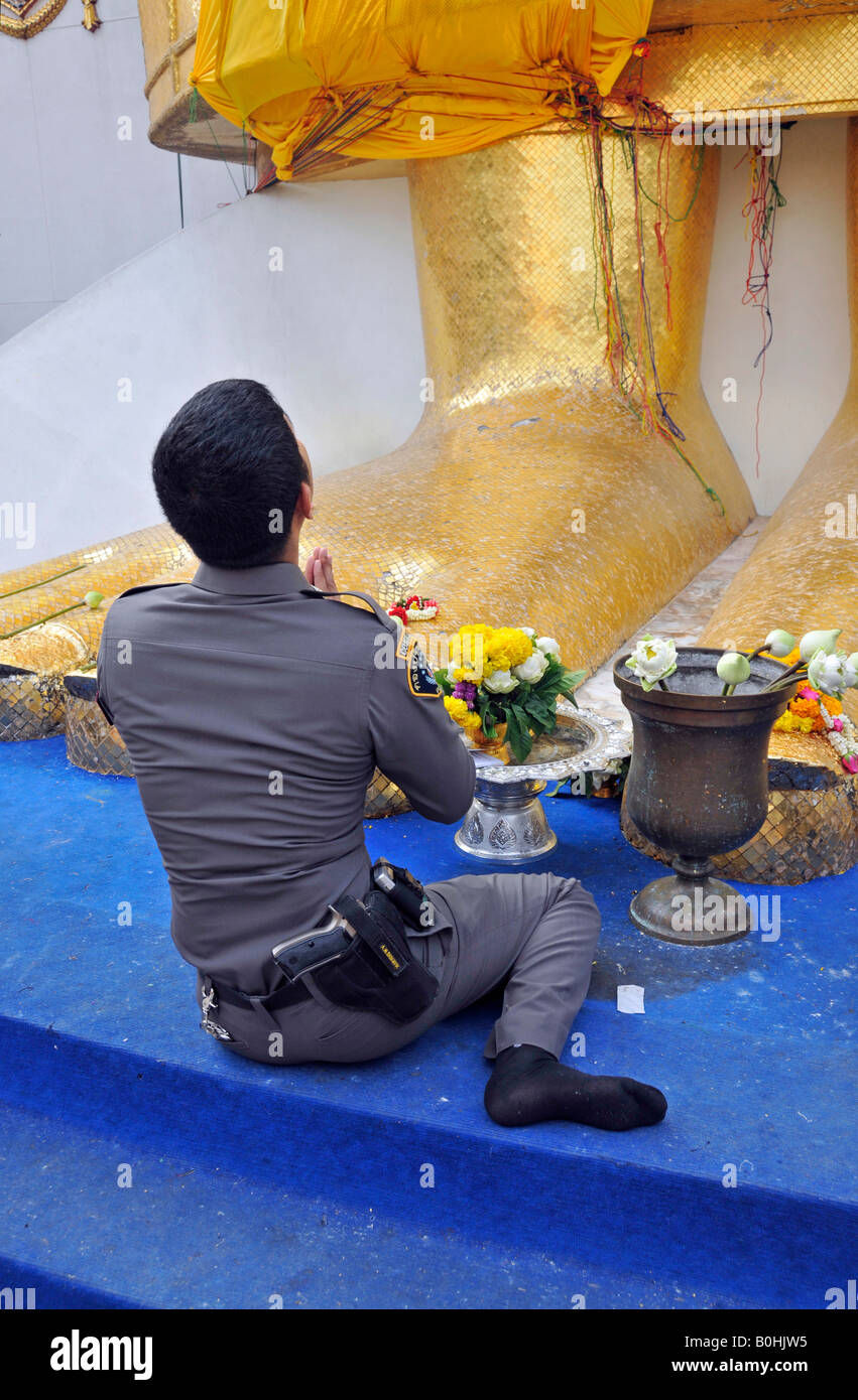 Poliziotto pregando presso il gigante i piedi di una statua dorata, Wat Intrawihan tempio, Bangkok, Thailandia, Sud-est asiatico Foto Stock