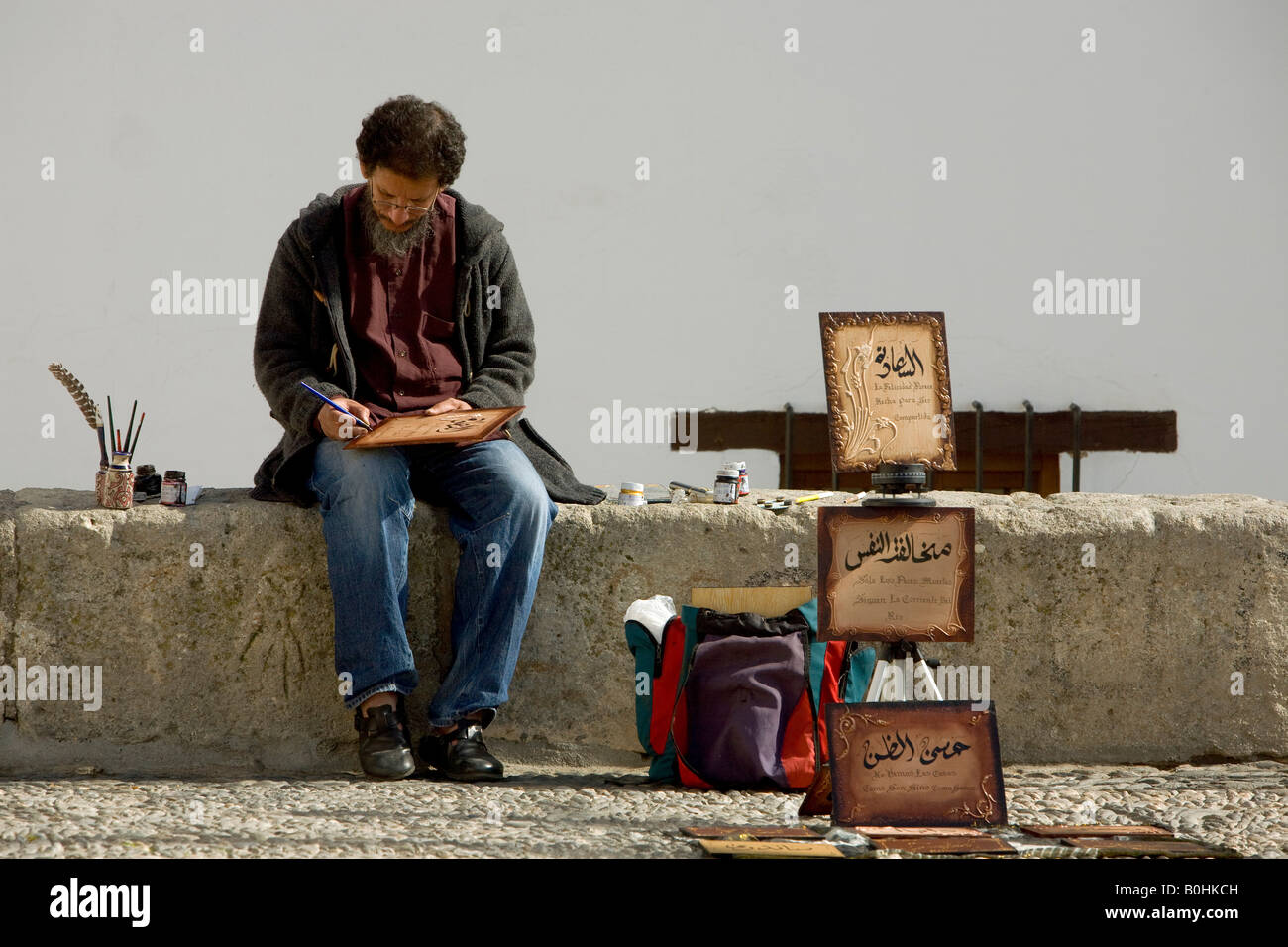 Uomo arabo vendita di calligrafia seduta sul Mirador San Nicolas in El Albayzín o quartiere Albaicín di Granada, Andalusia, S Foto Stock