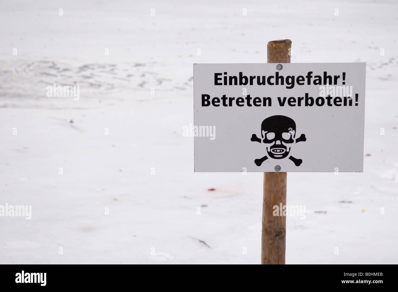 Segnale di avvertimento con Teschio e Ossa Croce, 'Dira di rottura attraverso il ghiaccio! Nessuna trasgressione' posted in un lago ghiacciato Foto Stock