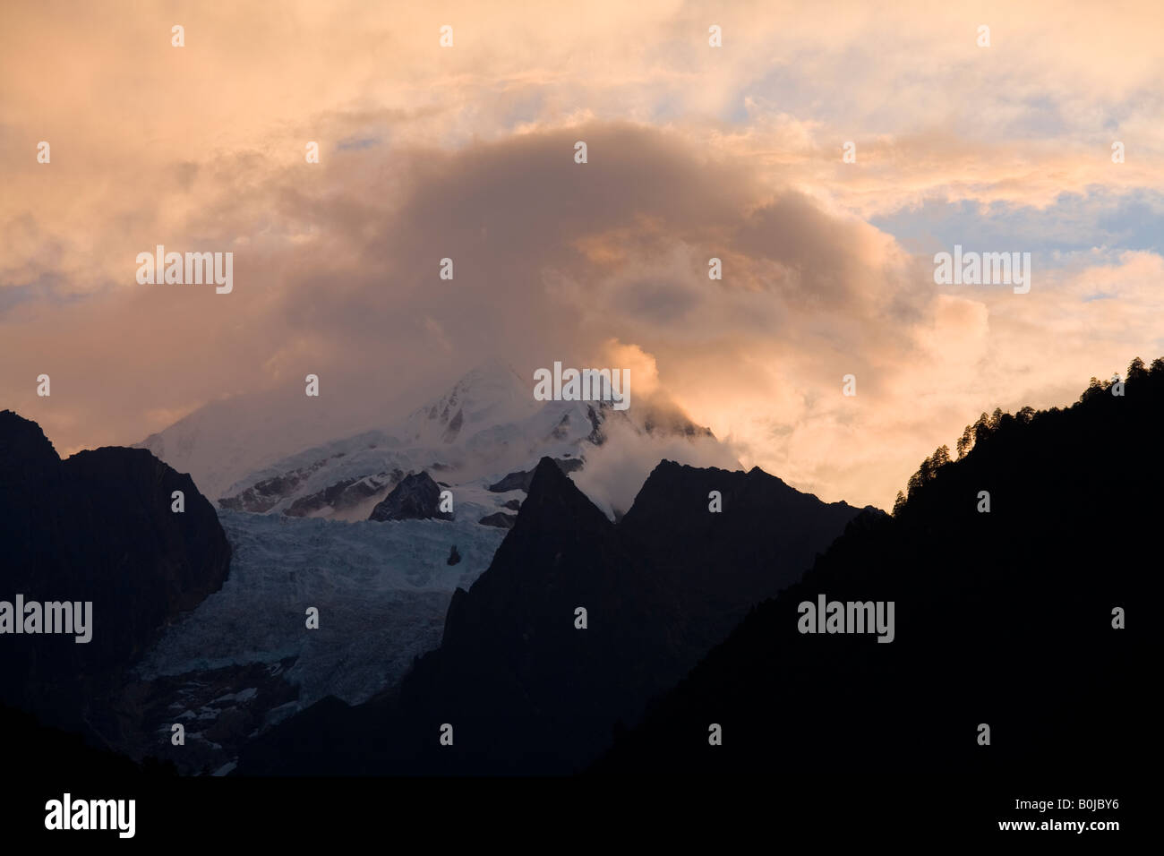 Golden Sunset over Gongga Shan in montagna Hailuogou Glacier Park / nazionale dei Geoparchi con boscose pendici di fronte del ghiacciaio Foto Stock