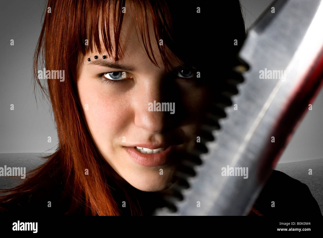 La ragazza con i capelli rossi tenendo un coltello contro la fotocamera con un male sorriso sul suo viso Studio shot Foto Stock