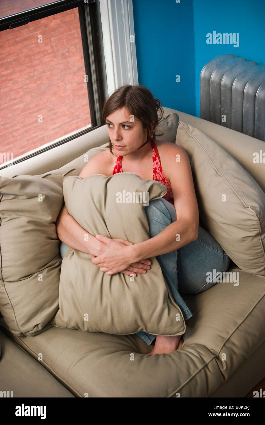 Giovane donna seduta sul suo divano modello rilasciato Foto Stock