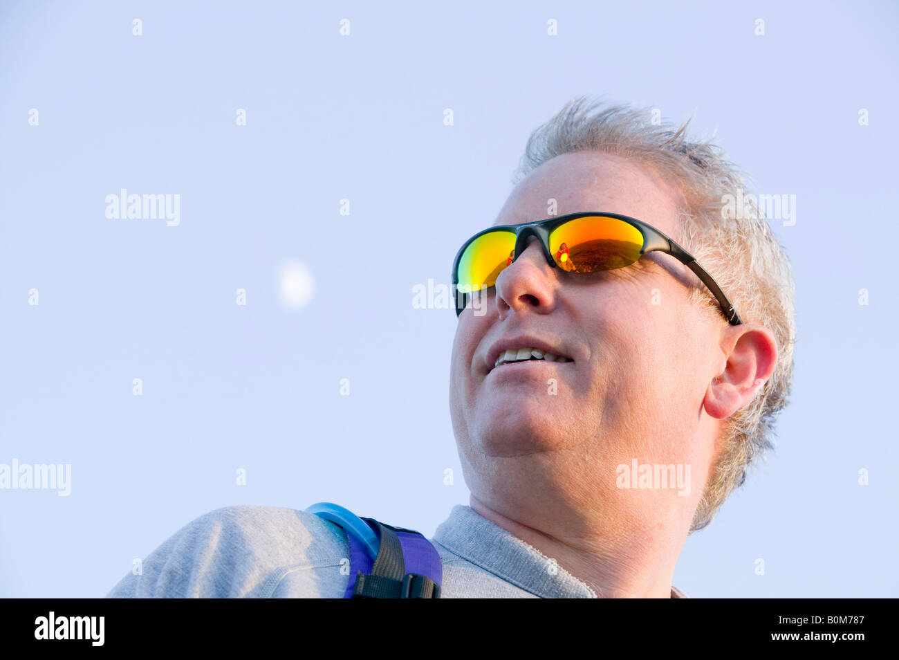 Un uomo che riflette i suns energia con una parabola riflettente in cima a una montagna nel distretto del lago UK si riflette in un mans occhiali da sole Foto Stock