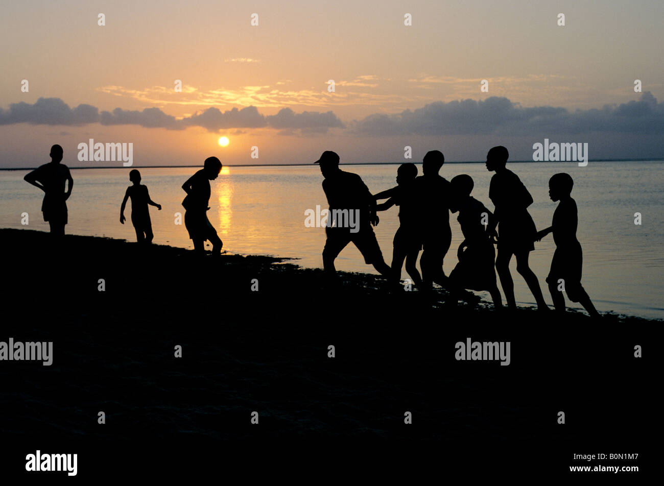 Un gruppo di giovani ragazzi africani su Bazaruto Island giocando sulla spiaggia stagliano contro una regolazione del sole Foto Stock