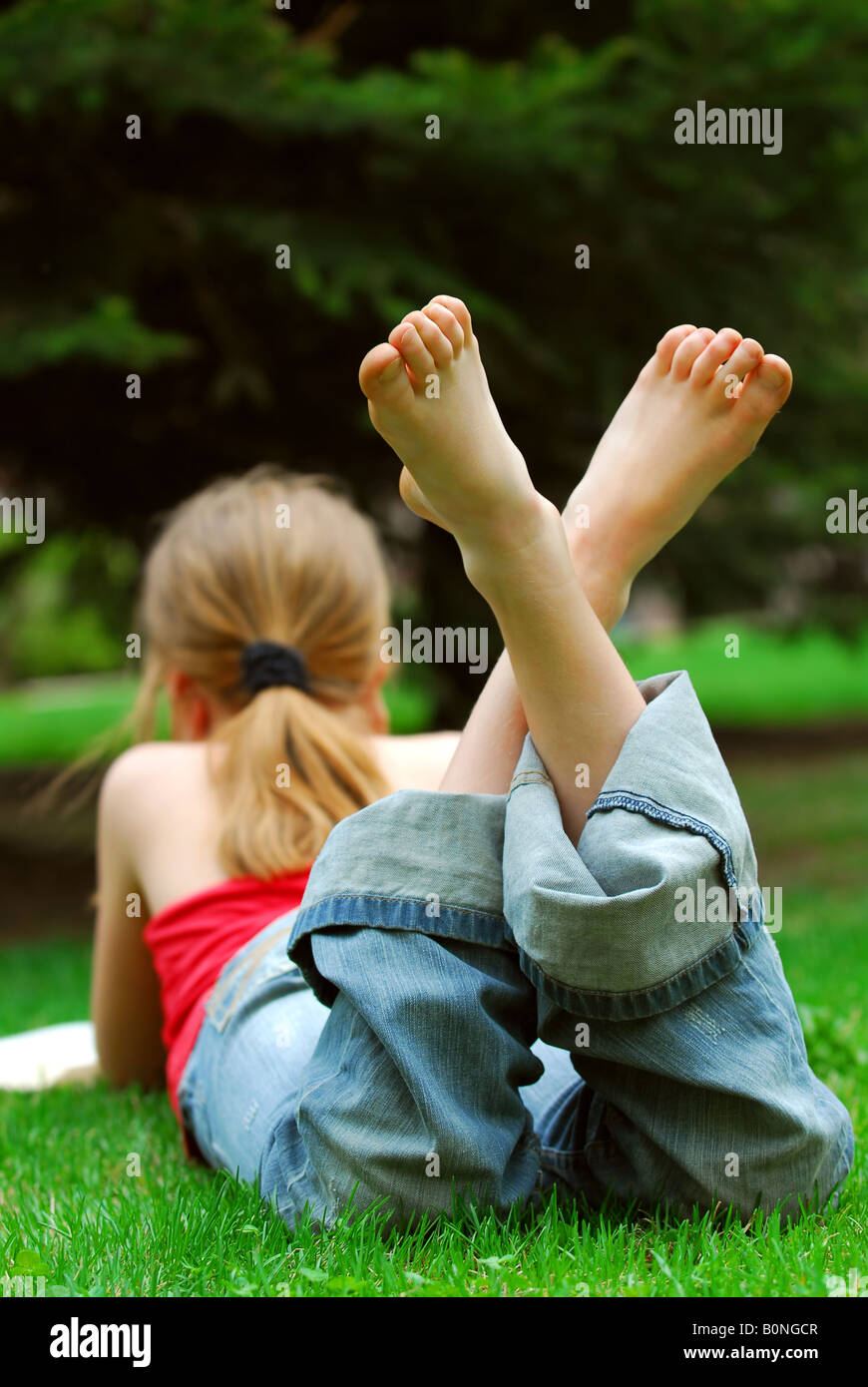 Giovane ragazza rilassante con un libro su erba verde in un parco di estate Foto Stock