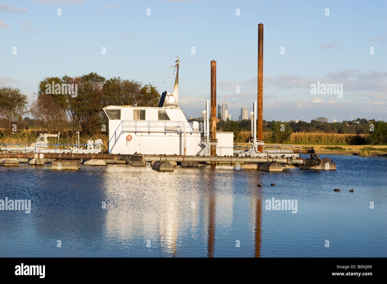 Un rimorchiatore di alta tecnologia per la rimozione di limo al Lago di pastore, Perth. Perth la grattacieli si vede dietro la draga Foto Stock