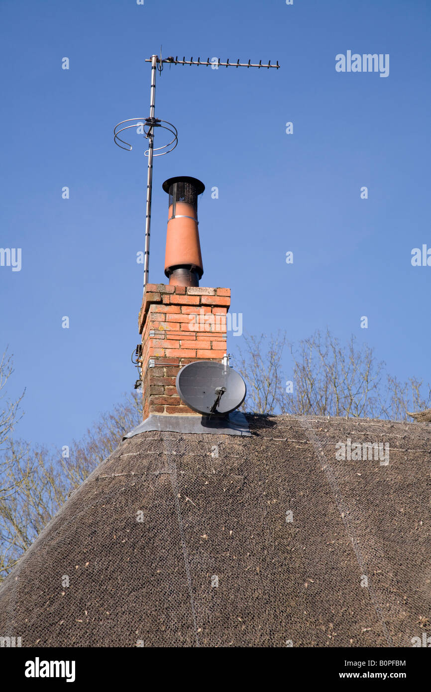 Parabola satellitare su un tetto di paglia accanto ad un camino montato TV  antenna ariel Foto stock - Alamy